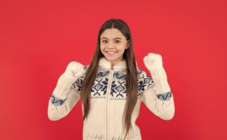 positive teen girl in warm winter knitted mittens and sweater in studio. teen winter girl isolated on red background. warm winter knitwear fashion.