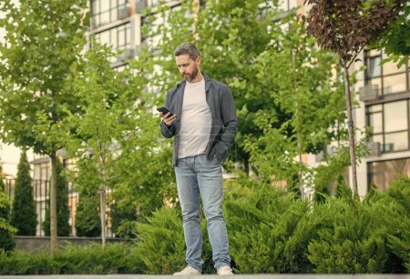 Photo for Full length of man chatting on phone outdoor. man chatting on phone in the street. man chatting on phone outside. photo of man chatting on phone in hands. - Royalty Free Image