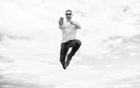 man jumping and presenting smartphone on sky background.