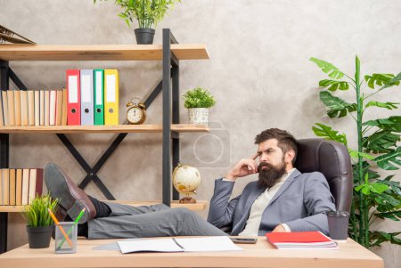 Pensativo hombre de negocios relajarse con las piernas en el escritorio de la oficina, descanso de trabajo.