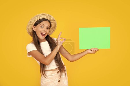 amazed teen girl with copy space on green paper on yellow background. ok.