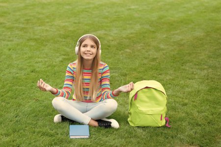 Téléchargez les photos : Méditer fille écouter de la musique assis sur l'herbe après l'école, éducation. - en image libre de droit