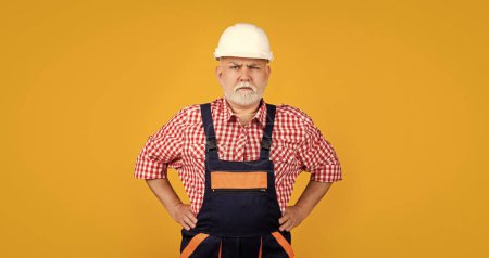 serious mature man builder in helmet on yellow background.