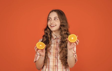 positive teen child hold citric fruit on orange background.