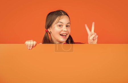 glückliches Kind hinter leerem orangefarbenem Papier mit Kopierplatz für Werbung. Frieden.