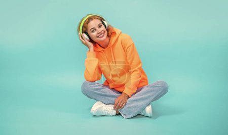 image of woman has music lifestyle wear headphones. woman has music lifestyle isolated on blue. woman has music lifestyle in studio. woman has music lifestyle on background.