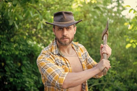 cowboy threaten with axe outdoor. photo of cowboy with axe. cowboy with axe. cowboy with axe wearing checkered shirt.