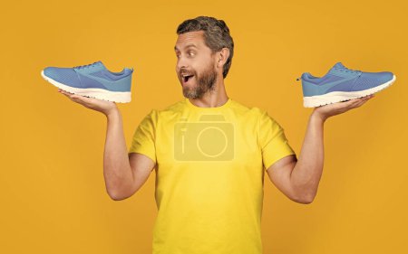 image of amazed fitness man with sneakers shoes. fitness man with sneakers isolated on yellow. fitness man with sneakers on background. fitness man with sneakers in studio.