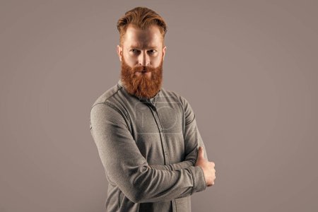 Confident Irish guy. Bearded guy with beard and mustache. Serious unshaven guy keeping arms crossed studio isolated on grey.