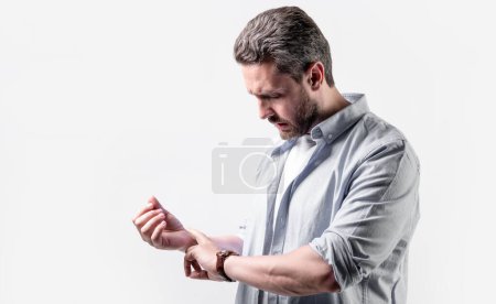 mature man with pulse on wrist, copy space. man check pulse on wrist isolated on grey background. man checking pulse on wrist in studio. photo of man measuring pulse on wrist.