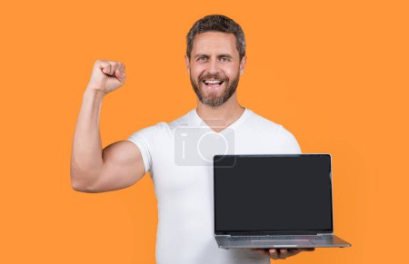 happy man showing laptop app in studio. man showing app on laptop. man showing app on screen with copy space. man showing app isolated on yellow background.