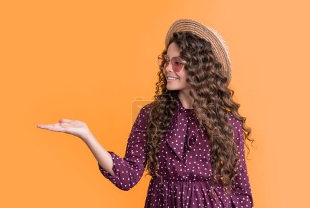 smiling girl in straw hat and sunglasses with long brunette curly hair on yellow background.
