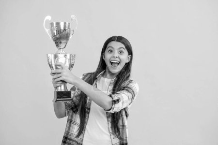 glad teen girl accept award on background. proud teen girl with champion cup award. teen girl hold her award champion cup isolated on yellow. teen girl receive award in studio.