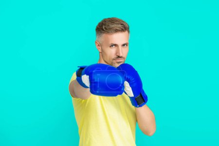 Strong boxer in sportswear. Exercising and punching. Practicing boxing. Sportsman in boxing gloves isolated on blue. Mature man boxer. Sport man boxing. Strong athlete man. Sportsman in gym. Knockout.