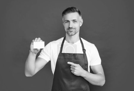 smiling mature man in apron with copy space on card. pointing finger.