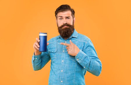 confused brutal bearded man point finger on shampoo bottle on yellow background, skincare.