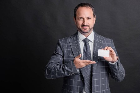 business man showing card presenting product in studio. man holding business card with copy space. photo of business man with card. business man with card isolated on black background.