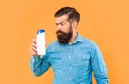 brutal bearded man hold hair conditioner bottle on yellow background, haircare.