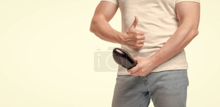Guy crop view giving thumb holding eggplant at crotch level imitating erect penis isolated on white, copy space.