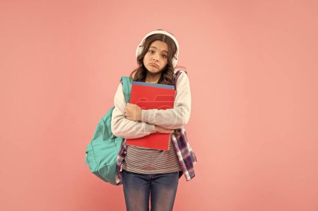 sad child in earphones hold workbook and backpack. online education. back to school. teen girl in headphones. listen to music. wireless audio device accessory. new technology. childhood development.