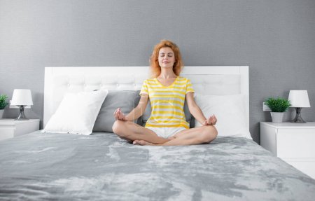 Mujer relajada meditando sentada en posición de loto en la cama, meditación. Chica meditativa en relajarse en el dormitorio. Práctica de meditación. Meditación para relajarse.