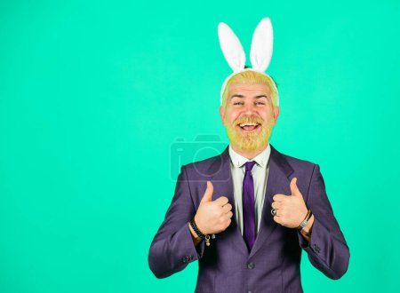 Sortez votre lapin intérieur. Lapin de Pâques. Un homme d'affaires heureux porte des oreilles de lapin. L'homme barbu montre les pouces levés. Soirée déguisée de lapin. Accessoire de vacances festive. Célébration de Pâques, espace copie.