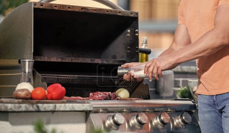 Homme de plein air cuisson grill et barbecue plats. Homme griller des steaks à la perfection sur barbecue fumé. Le grilleur fait cuire la viande au barbecue. Délicieuses viandes grillées. b?uf rôti.