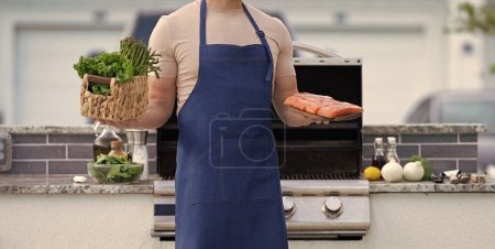 Photo for Cropped photo of bbq man with salmon fish. bbq man with salmon fish. bbq man with salmon fish outdoor. bbq man with salmon fish in apron. - Royalty Free Image