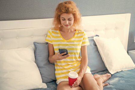 cheerful woman with coffee shopping online on phone. woman shopping online at home with phone. online shopping at home of woman.
