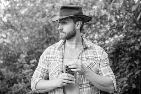 Photo for Western man with whiskey flask outdoor. western man with whiskey flask wear checkered shirt. photo of western man with whiskey flask. western man with whiskey flask. - Royalty Free Image