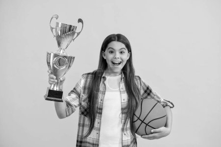 amazed teen basketball girl hold her award cup isolated on yellow. teen basketball girl receive award in studio. teen basketball girl accept award. proud teen basketball girl with champion cup award.