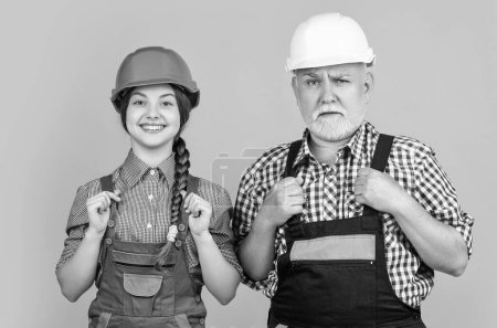 child and grandfather builder in helmet on yellow background.