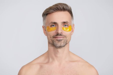 Eye patch. Beauty man face with under eye collagen pads. Mature man has fresh healthy skin with collagen patches under eyes. Facial treatment. Man applying eye patches. Spa care. Skincare routine.