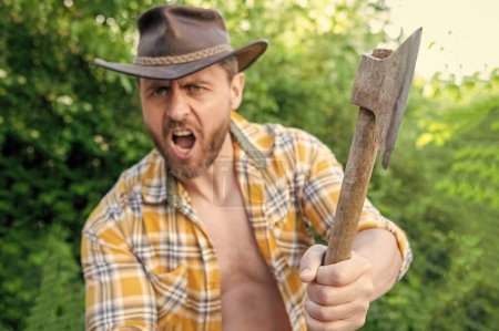 selective focus of angry lumberjack with axe. angry lumberjack with axe wearing checkered shirt. angry lumberjack with axe outdoor. photo of angry lumberjack with axe.
