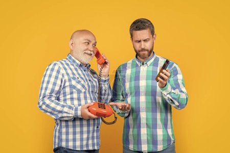 verblüffte Männer mit Telefonkontrastgesprächen im Studio. Männer mit Telefonkontrasten rufen im Hintergrund an. Foto von Männern mit Telefonkontrastgespräch. Männer mit Telefonkontrastruf isoliert auf gelb.
