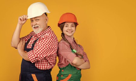 cheerful child and grandfather builder in hard hat on yellow background.