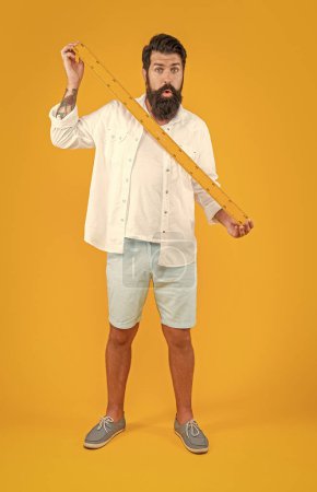 shocked man hold school ruler isolated on yellow. man hold school ruler in studio. man hold school ruler on background. photo of man hold school ruler.