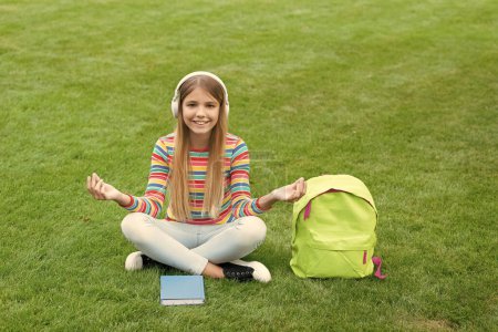 Téléchargez les photos : Meditating teen girl listening to music sitting on grass after school, education. - en image libre de droit
