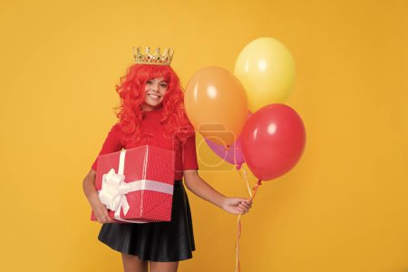 girl smile in crown with present box and party balloon on yellow background.