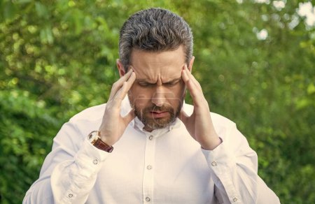 Stressed professional man suffering from headache natural background, fatigue.