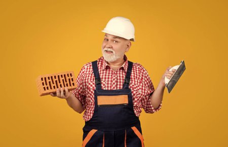 happy old man bricklayer in helmet on yellow background.