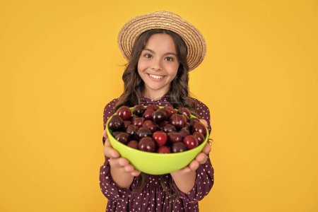 selective focus of cherry bowl in hands of happy teen child on yellow background.