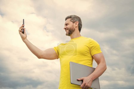 man with laptop having video call on smartphone on sky background.