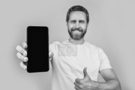Mann zeigt Smartphone-App auf gelbem, selektivem Fokus. Mann zeigt Smartphone-App im Hintergrund. Mann zeigt Smartphone-App im Studio. Foto von Mann zeigt Smartphone-App.