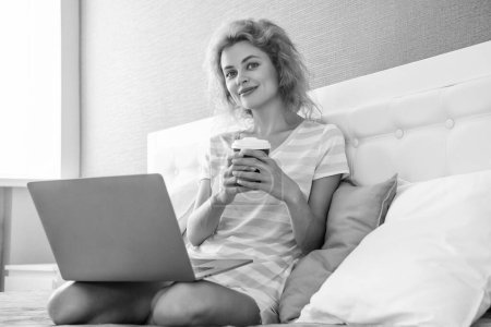 comunicación de chica sonriente con café y portátil. comunicación en línea de la chica en casa. comunicación portátil de chica en la cama con café.
