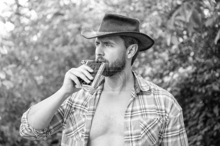 Photo for Cowboy man drinking bourbon hipflask. man with bourbon hipflask outdoor. man with bourbon hipflask wear checkered shirt. photo of cowboy man with bourbon hipflask. - Royalty Free Image