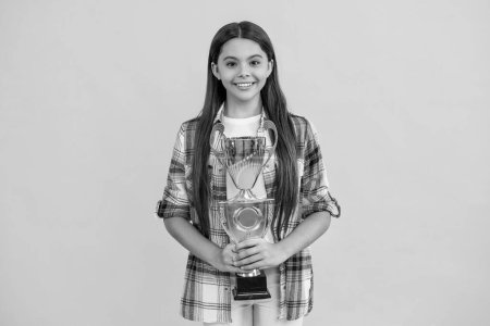 cheerful teen girl hold her award champion cup isolated on yellow. teen girl receive award in studio. teen girl accept award on background. proud teen girl with champion cup award.