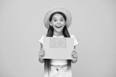 shocked teen girl hold empty advertisement paper with copy space on yellow background.