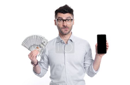 Doubtful guy showing cash money and smartphone. Guy feeling uncertain about paying in cash or by smartphone. Cash payment or smartphone payment. Cash purchase.