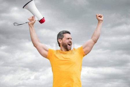man in yellow shirt shout holding loudspeaker on sky background.